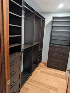 Custom-built walk-in closet with dark wood shelving and drawers, featuring multiple open shelves, a hanging rod area, and a set of soft-close drawers on both sides, all installed over a warm-toned bamboo floor.